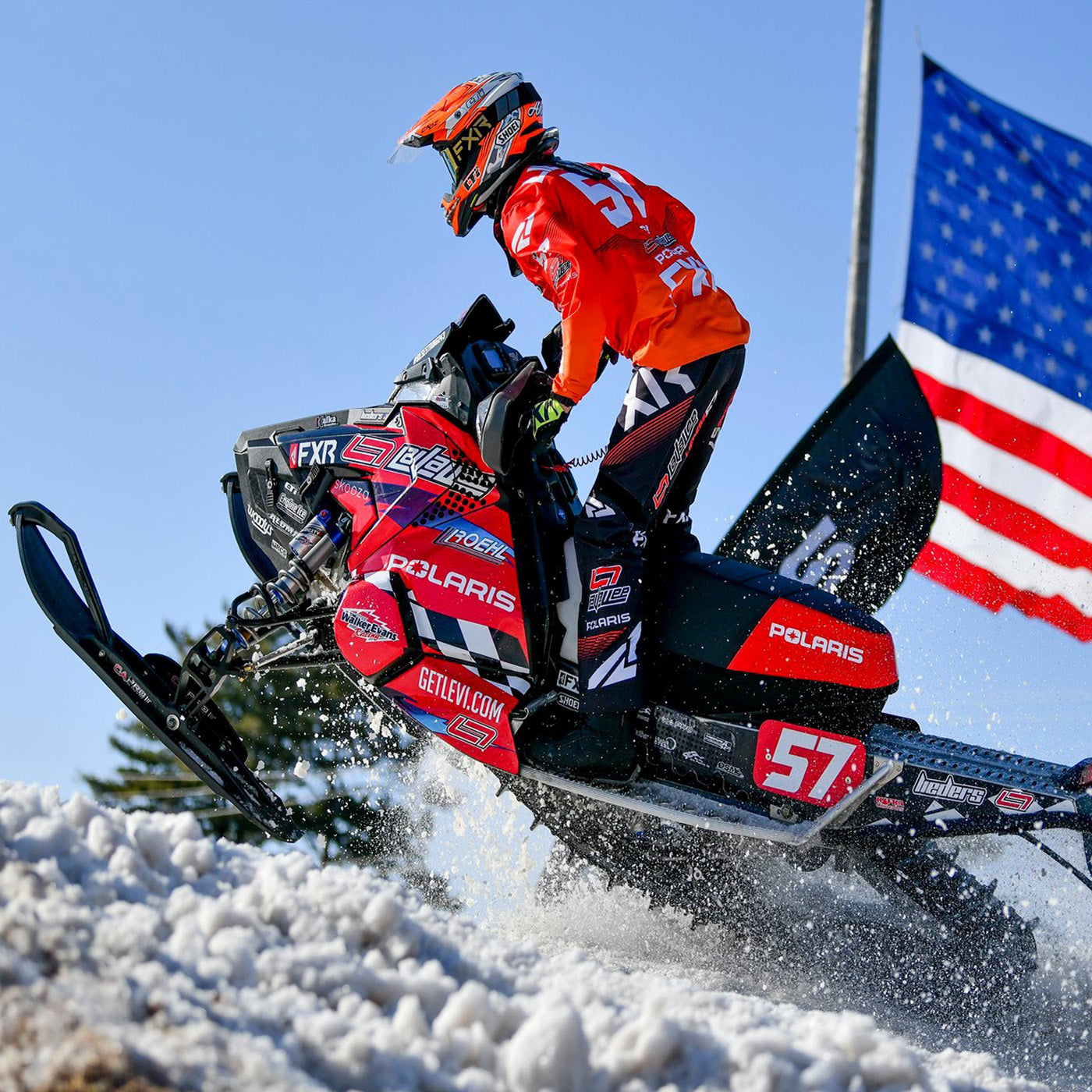 #57 Andy Lieders on a snowmobile speeding past an American flag with all-black C&A Pro skis. 